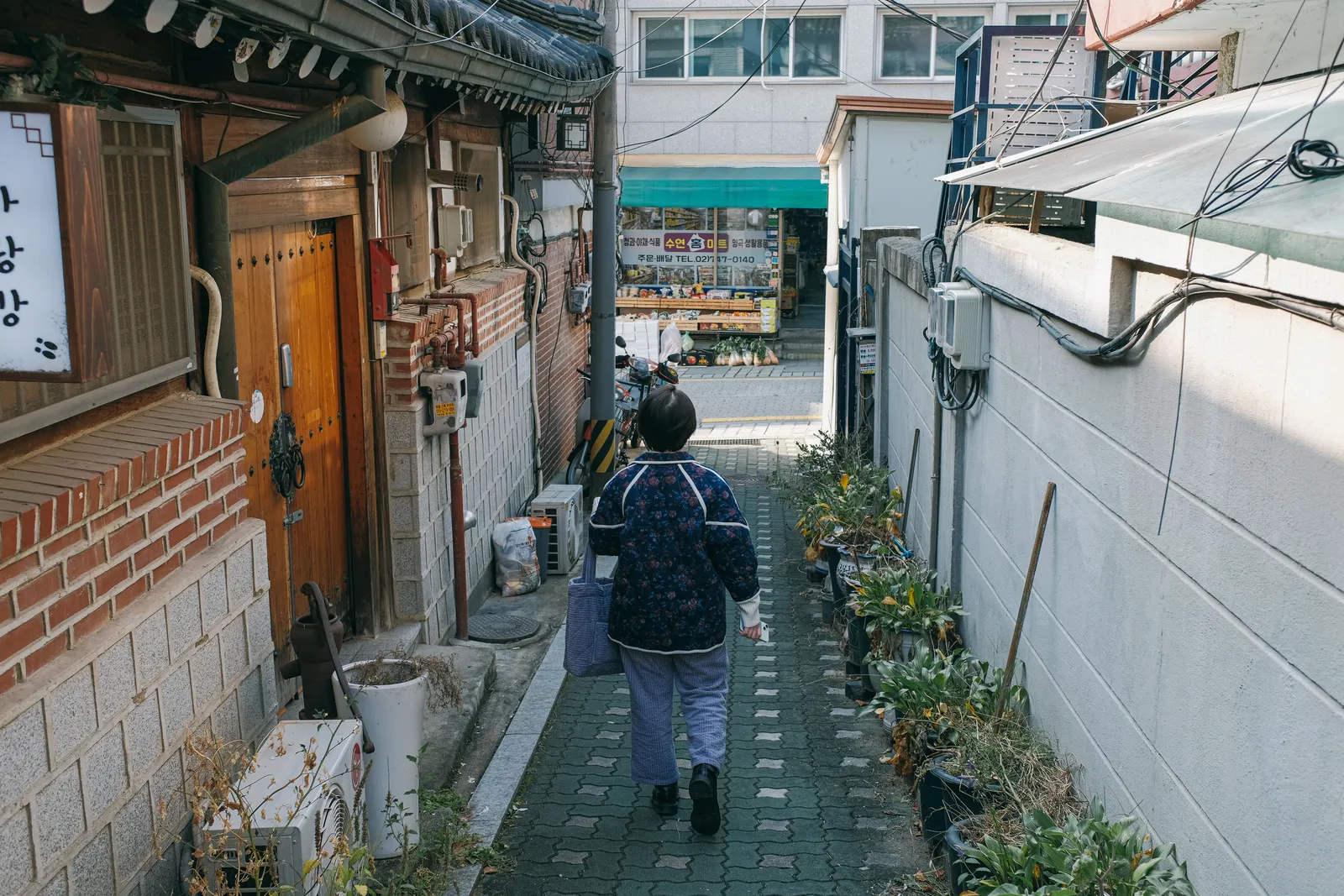A steep alley between traditional hanok walls with a person walking in Bukchon, Seoul