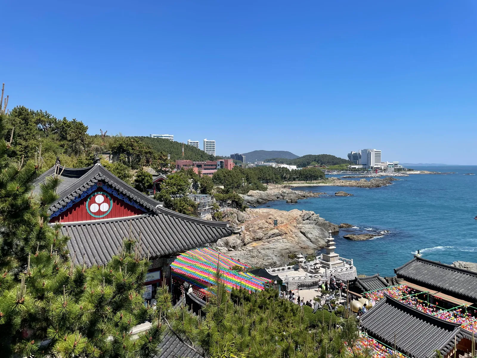 A wide sandy city beach backed by tall towers with people swimming under a summer sky in Busan, South Korea