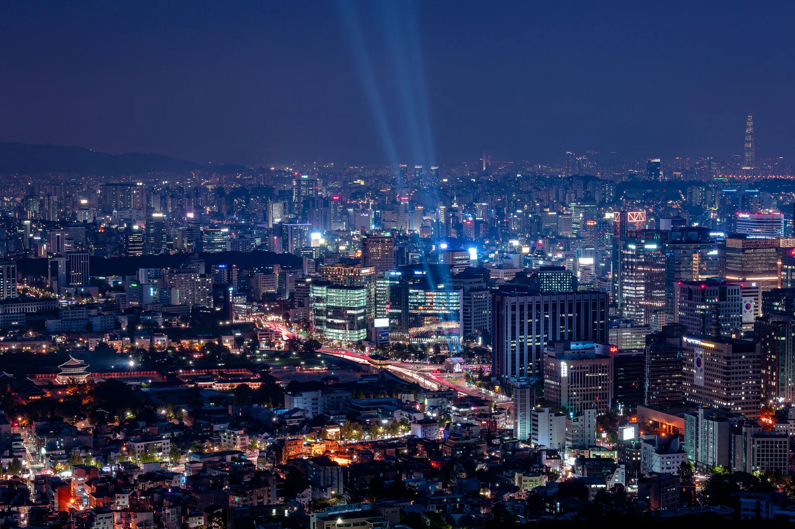 A restored royal palace with sweeping tiled roofs framed by modern towers in central Seoul, South Korea