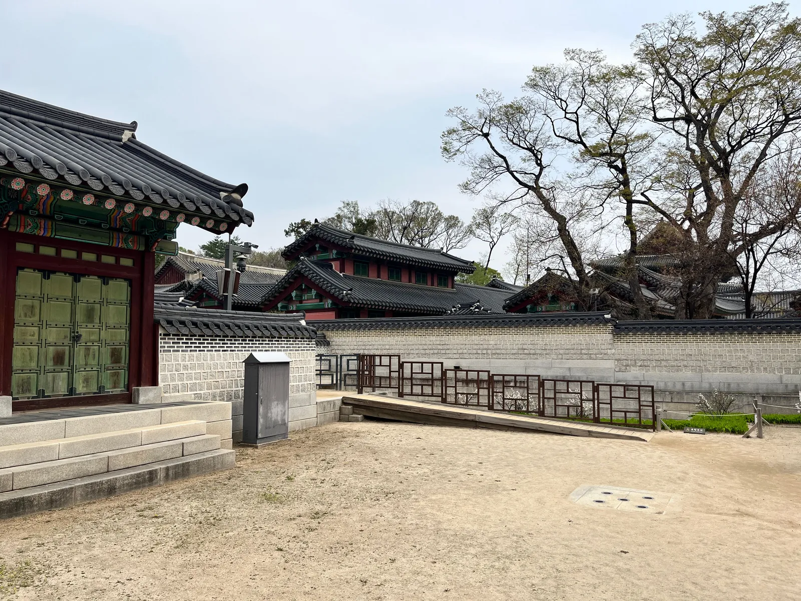Traditional palace buildings behind a stone wall with bare trees in Seoul, South Korea