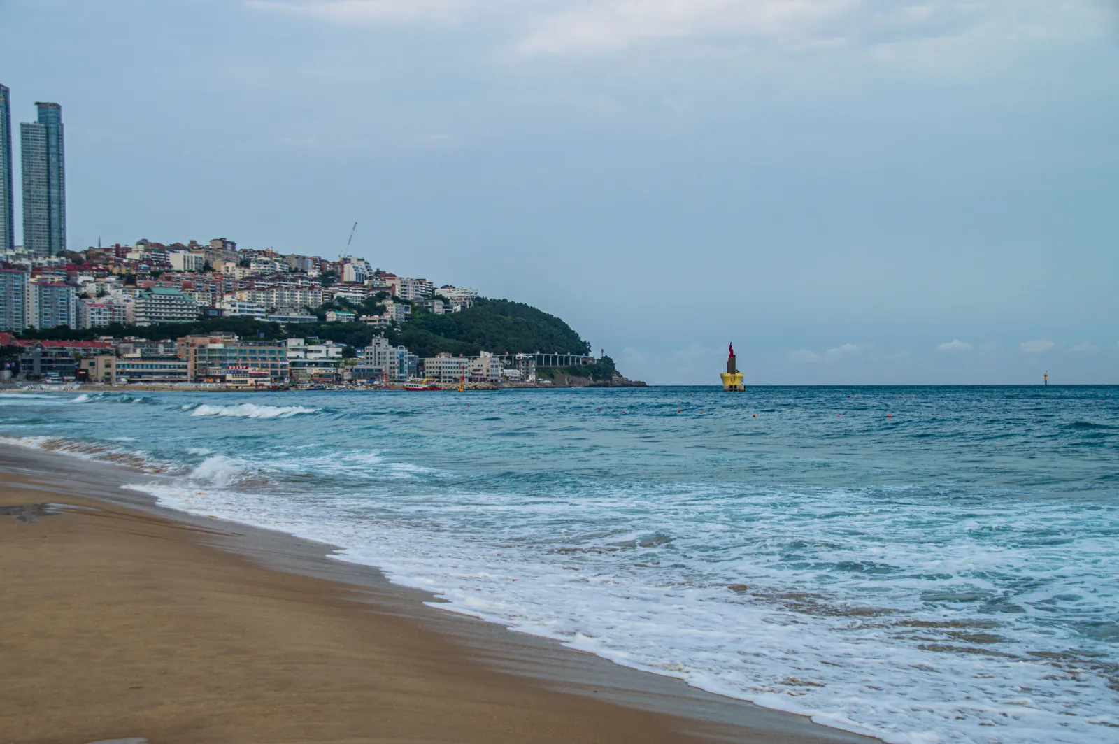 A curving sandy beach with a wooded headland at the far end in Busan, South Korea