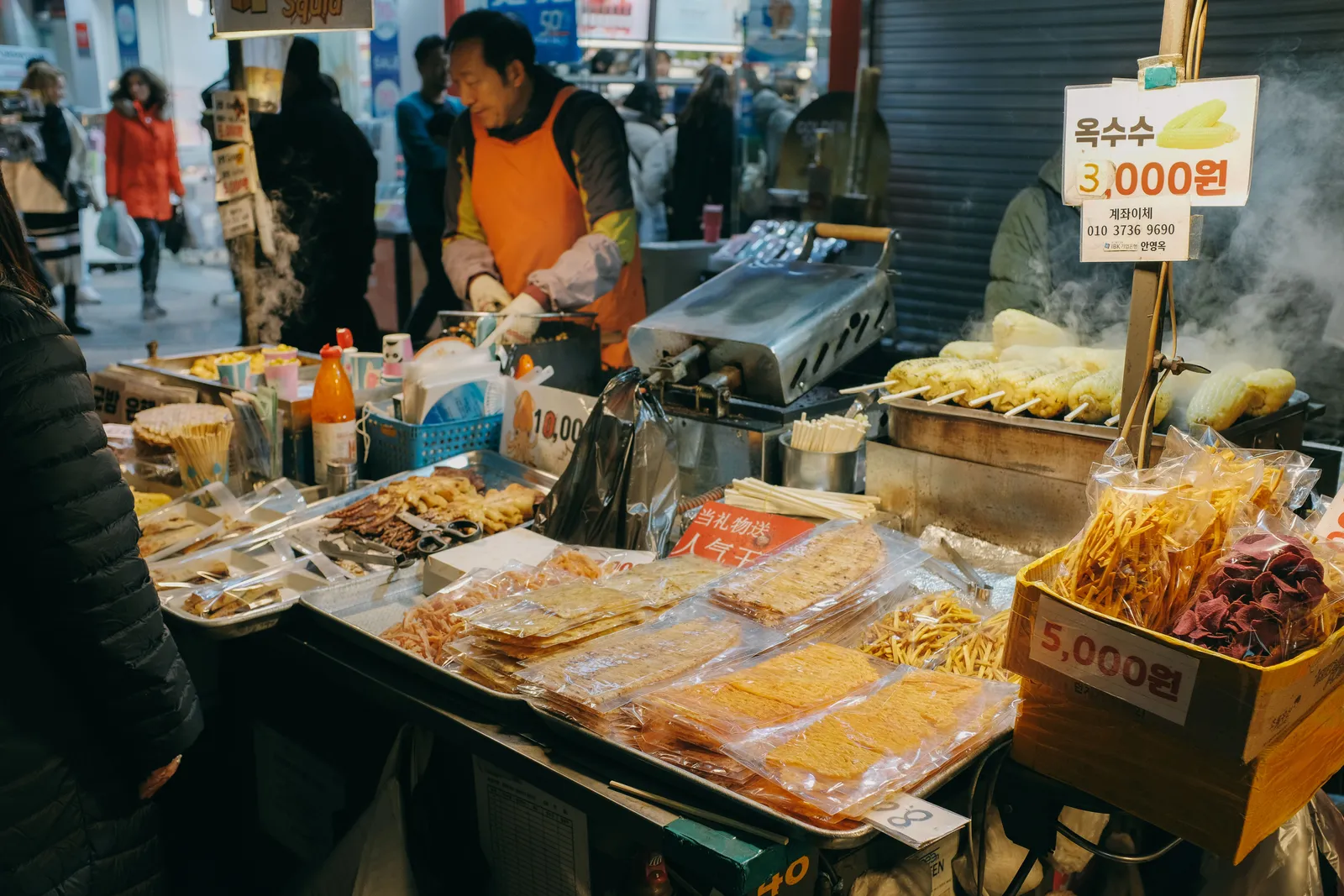 A steaming street food stall with a vendor serving customers at night, Seoul, South Korea