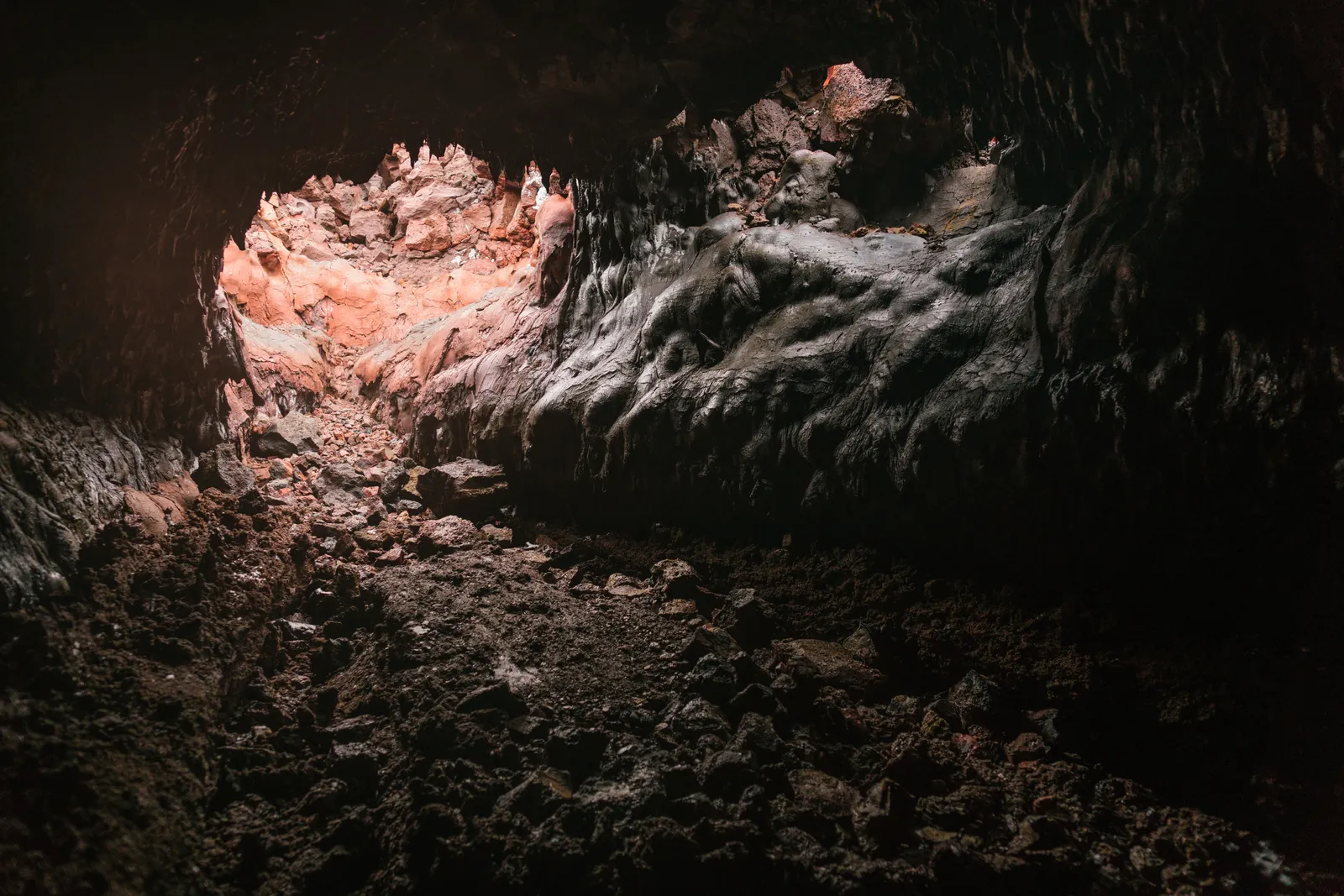 The rough basalt walls and uneven rock floor inside a lava tube, lit in the darkness