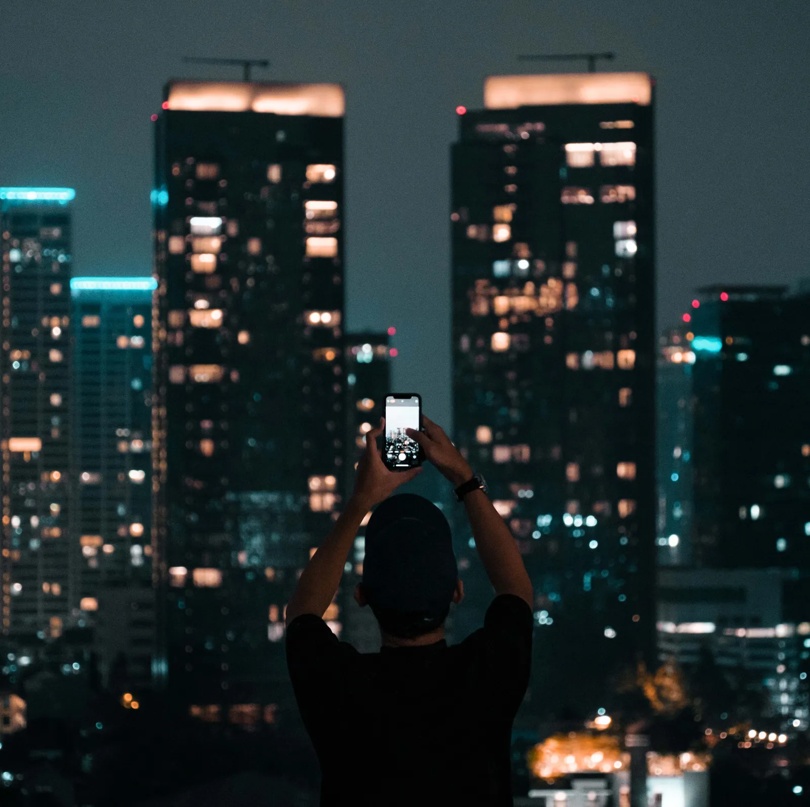A person photographing a lit city skyline at night in Seoul, South Korea