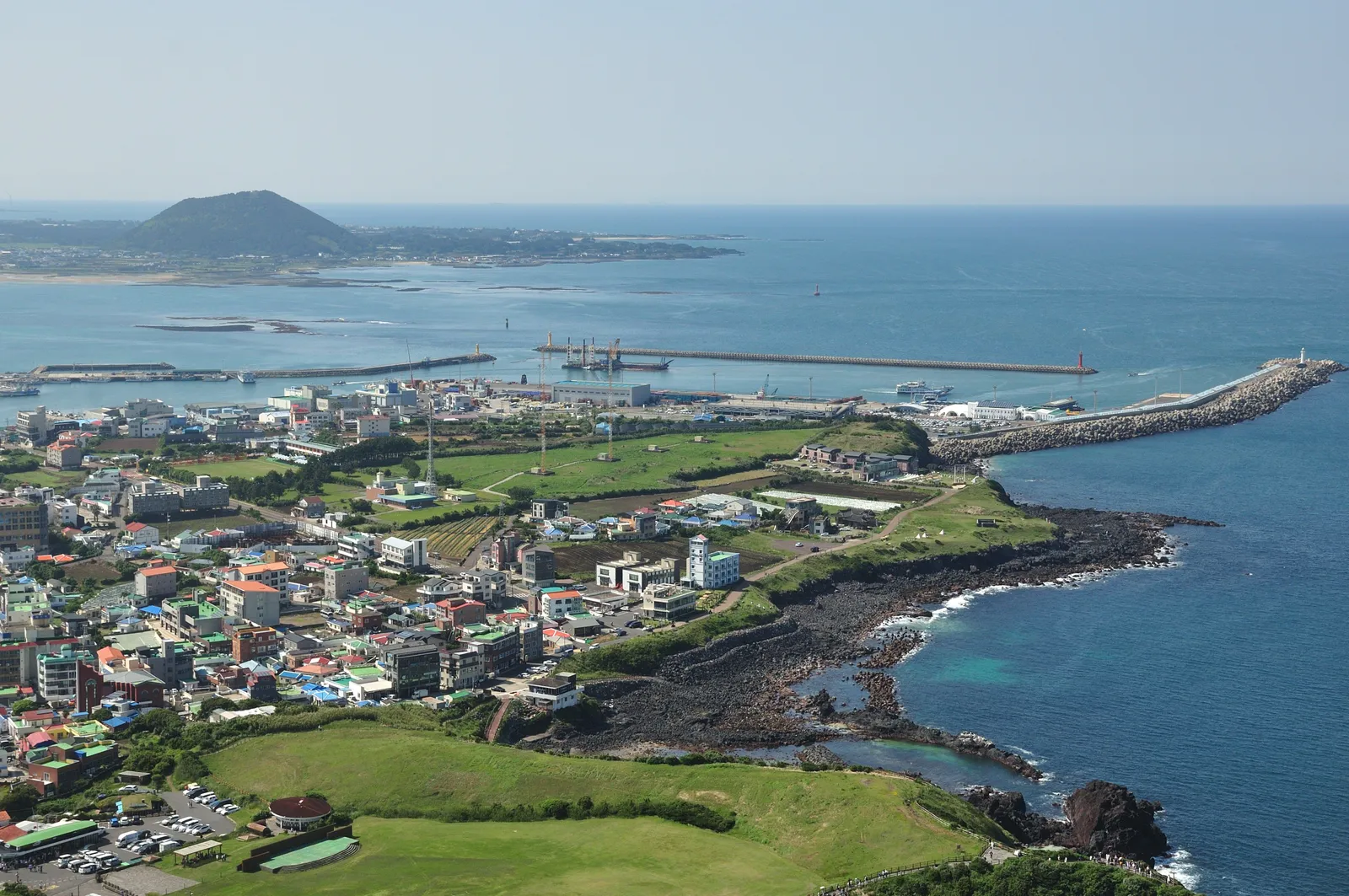 An aerial view of the Jeju coastline with fields, a village and a volcanic cone, South Korea