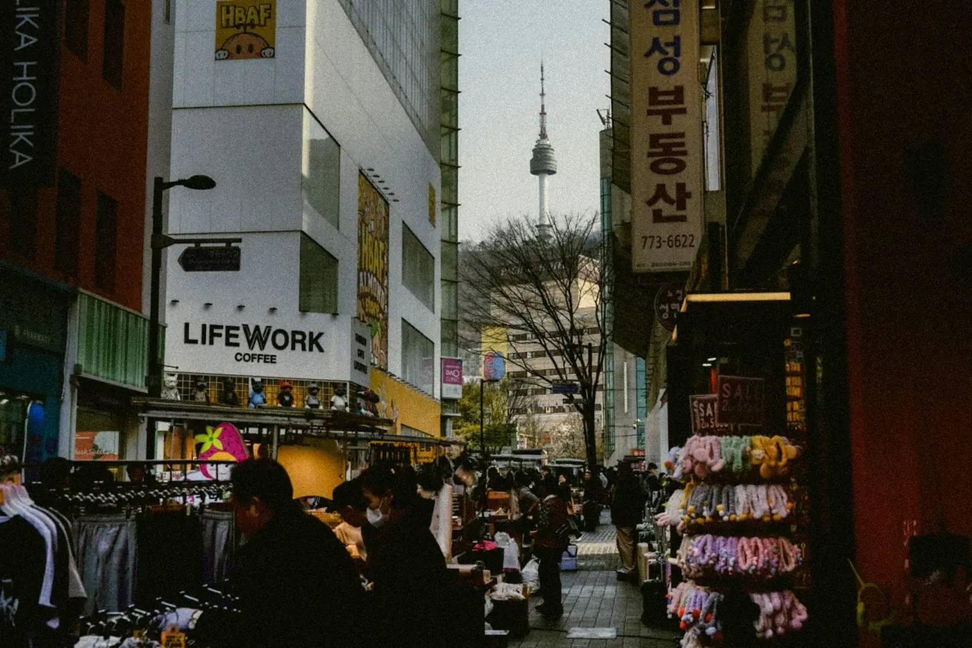 A busy shopping street in Seoul with market stalls and N Seoul Tower in the distance