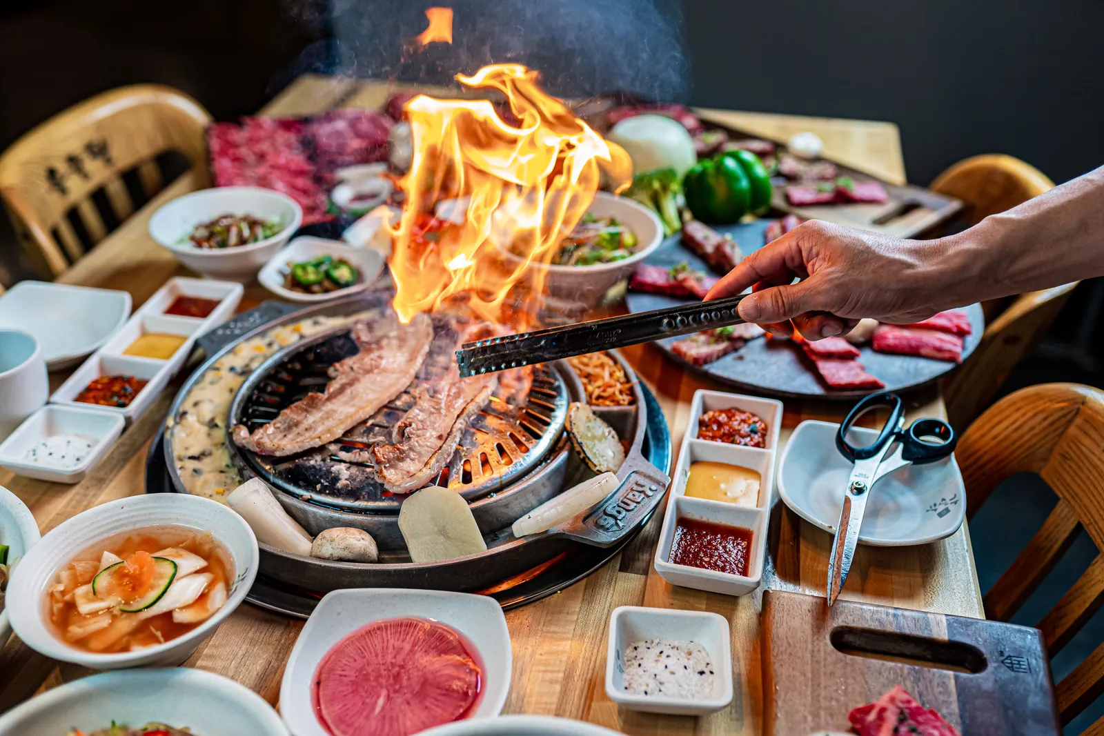 A charcoal grill loaded with sizzling Korean barbecue meat surrounded by small side dishes on a restaurant table, South Korea