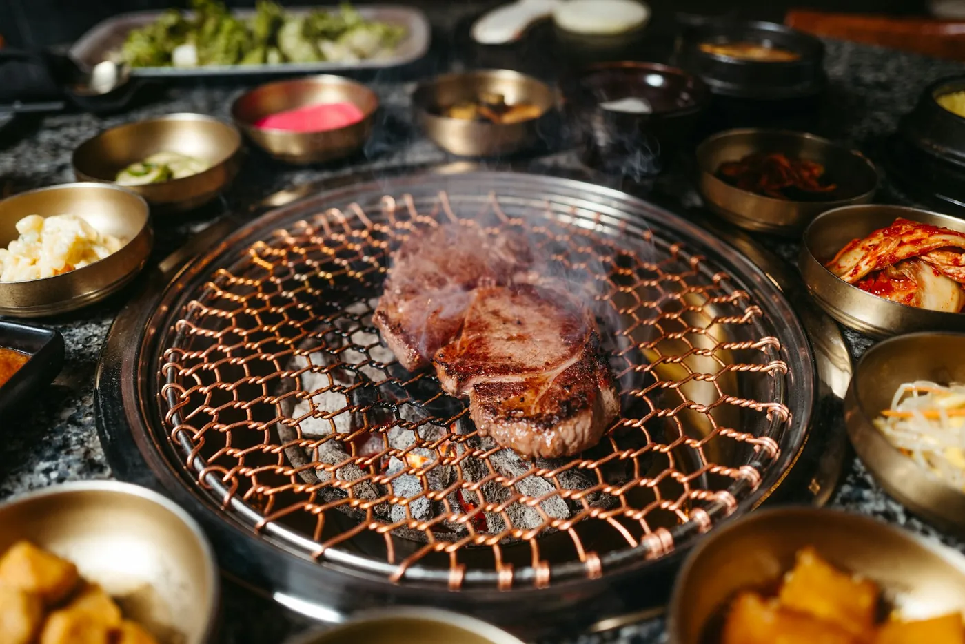 A staff member turning marinated short ribs on a tabletop grill at a Korean barbecue restaurant, South Korea