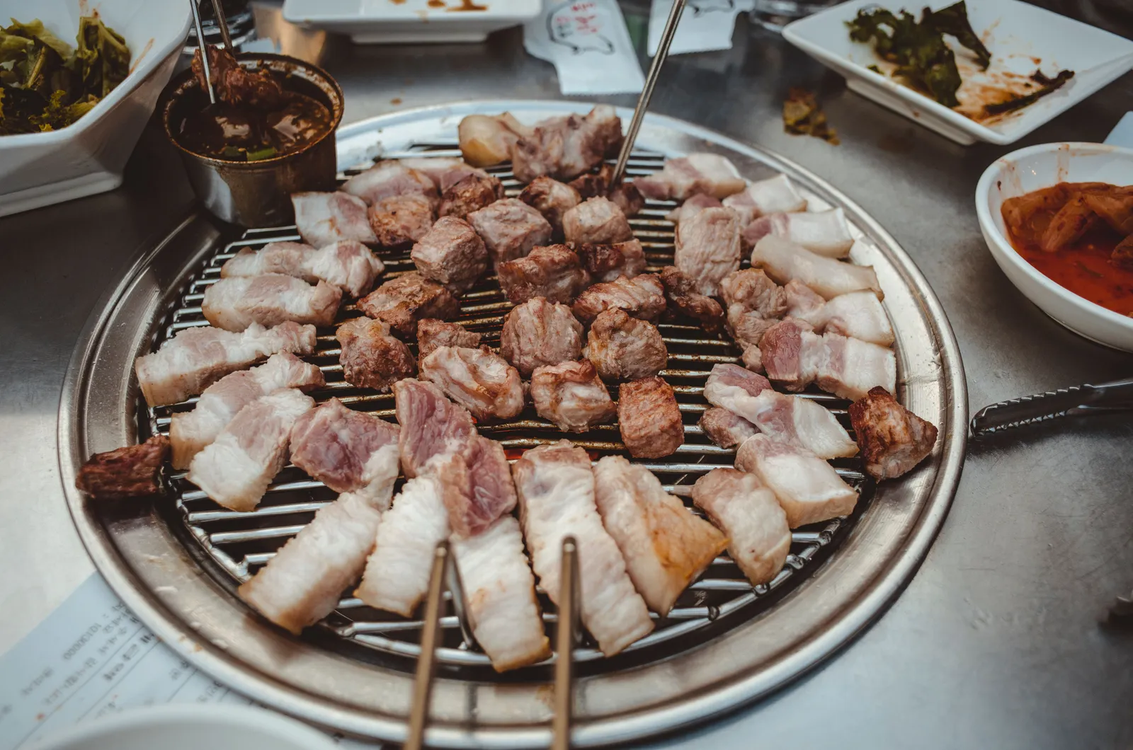 Grilled pork belly wrapped in a lettuce leaf with garlic and sauce, held over a table set for Korean barbecue, South Korea