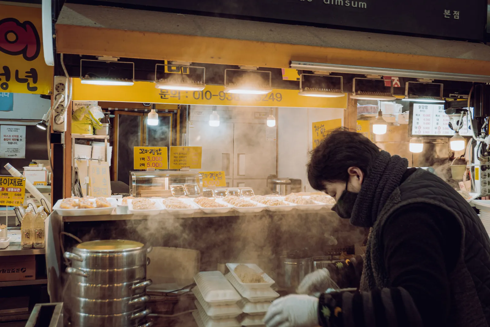 Rows of street food stalls with steam rising from cooking pans at a covered market in South Korea