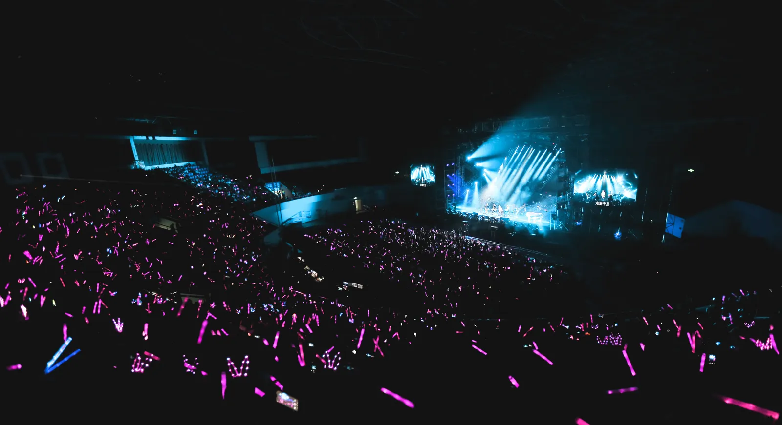 A concert crowd holding pink light sticks in front of a lit stage in South Korea