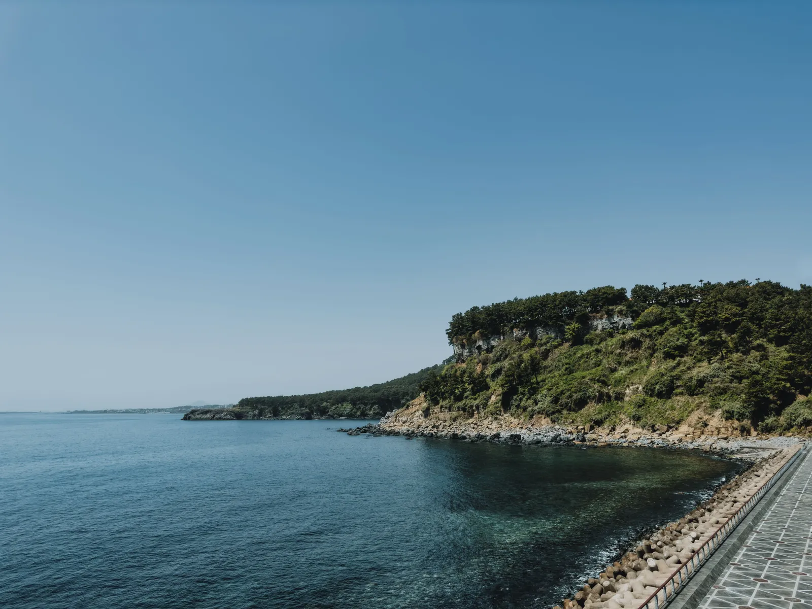 A coastal road and rocky shoreline with the sea beyond on Jeju island, South Korea
