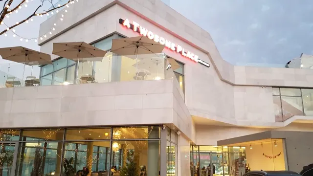 A pale cafe building with a terrace, umbrellas and a string of lights at dusk