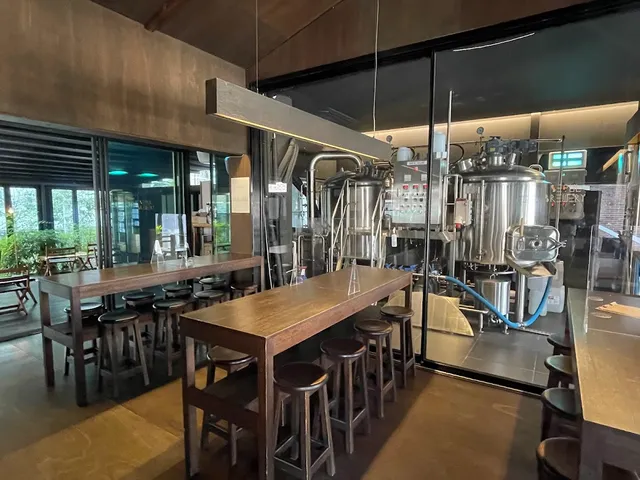 High wooden tables with stools, and stainless steel brewing tanks behind a glass wall