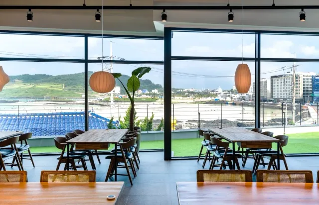 A dining space with a glass wall facing the sea, wooden tables and hanging paper lamps