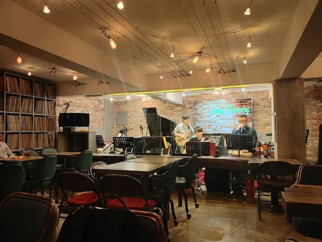 A band playing on a small stage with a piano, facing tables and shelves of records
