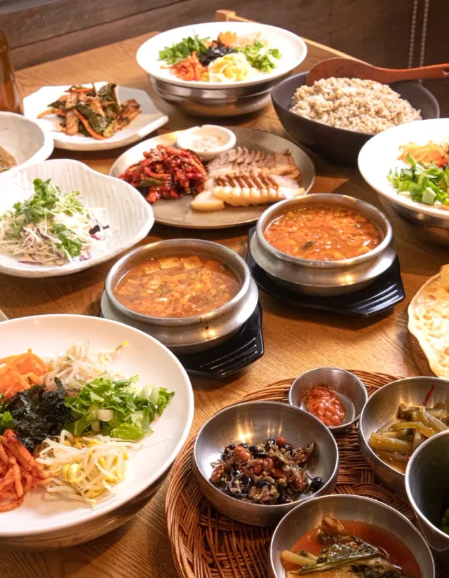 A table laden with vegetable bowls, barley rice, miso stews and many side dishes
