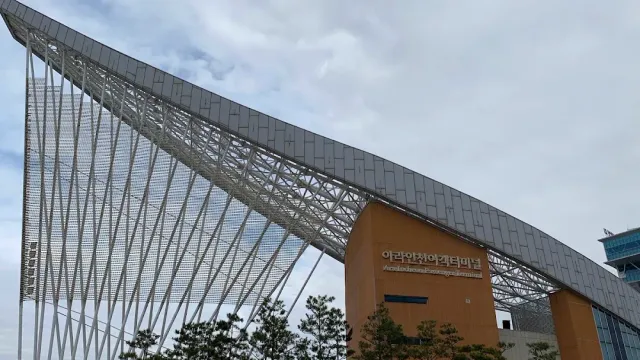 A modern building with a long curved metal roof held by thin cables