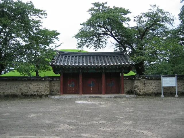 A red wooden gate in a stone wall with grassy green burial mounds rising behind it