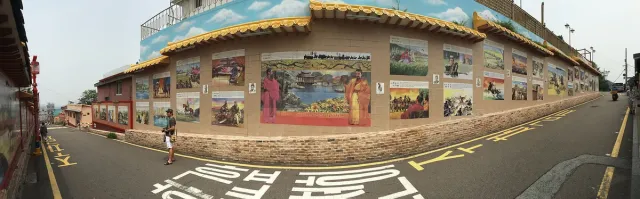 A street with a long wall covered in painted murals under a Chinese style tiled roof