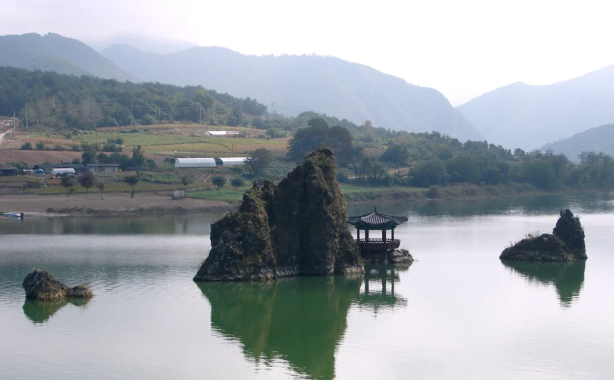 Three rock peaks rising out of a wide river, one of them crowned by a traditional pavilion