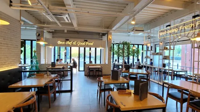 A bright hall with wooden tables, chairs, greenery and neon lettering on the wall