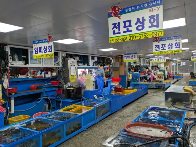 A fish market hall with blue tanks, hanging signs and a vendor in an apron