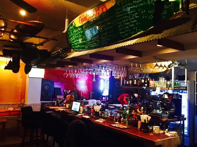 A colorful bar counter with hanging glasses, and a surfboard used as a menu board above it
