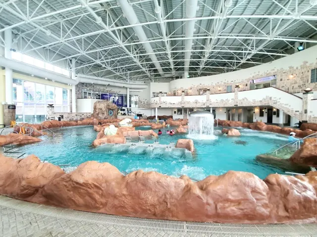 An indoor pool with artificial rocks, a waterfall and a high metal ceiling