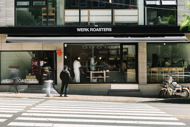 A black front with large windows, pedestrians at a crossing and a parked scooter