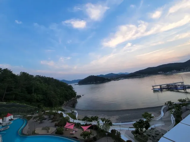 An elevated view over a calm bay and forested ridges at dusk, with a pool and a pier in front