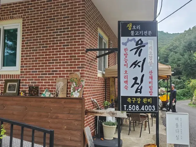 A corner of a brick building with a vertical sign, a wooden deck and planters by the road