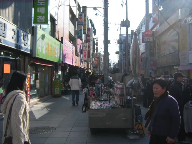 A narrow shopping street lined with shopfronts and signs, busy with pedestrians