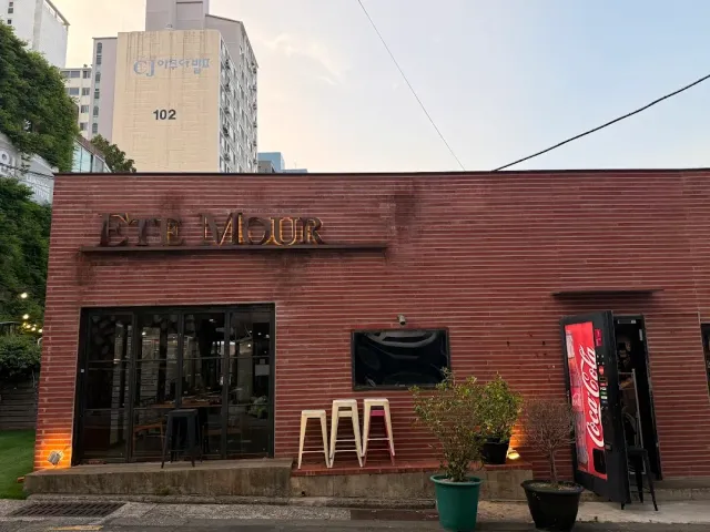 A red brick building with metal letters on the front, stools outside and a red vending machine