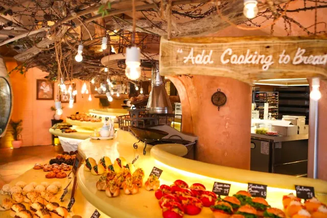 Curved pastry counters loaded with rolls, hanging bulbs and branches on the ceiling