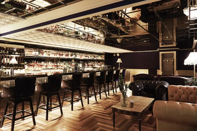 A long bar counter with high leather chairs, shelves of bottles and a herringbone wooden floor