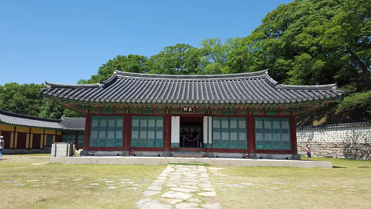 Traditional timber hall with a curved tiled roof, a stone path and lawn in front under a clear blue sky