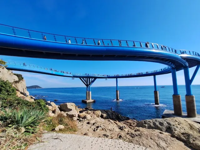 A curving blue walkway on pillars above the sea, visitors along it