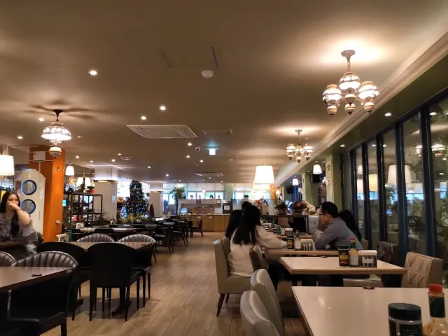 A spacious hall with chandeliers, a wooden floor, tables and diners beside tall windows