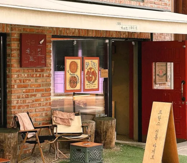 A brick front with pastry posters in the window, folding chairs and tree trunks used as stools