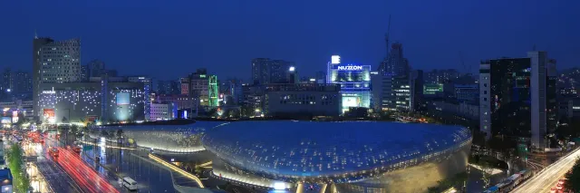 A curved gleaming metal building among city towers at dusk