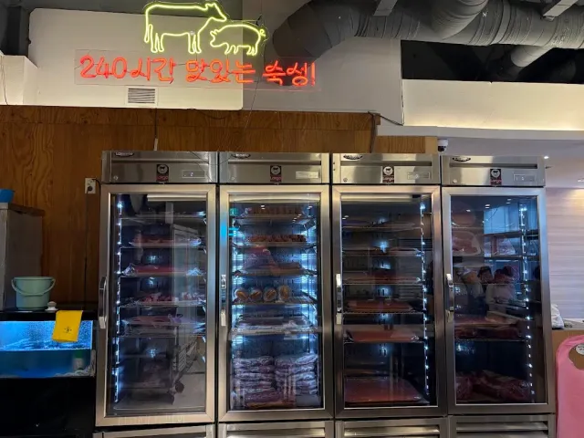 Lit glass refrigerators with cuts of meat for dry aging, and a neon sign of a cow and a pig above them