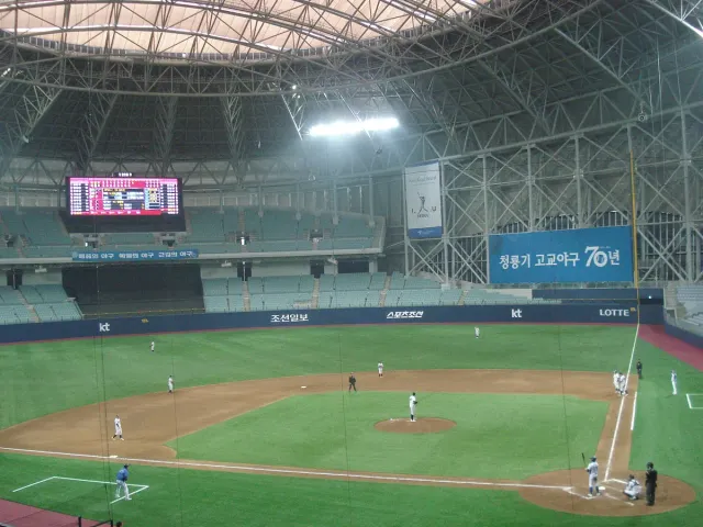An indoor baseball field with stands and a lit scoreboard