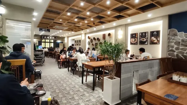 A hall with a coffered wooden ceiling, occupied tables and a stone wall hung with food photos