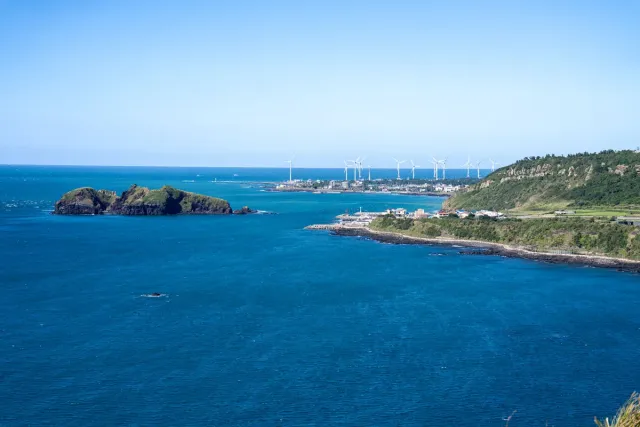 Deep blue sea with a green headland and a row of wind turbines on the horizon