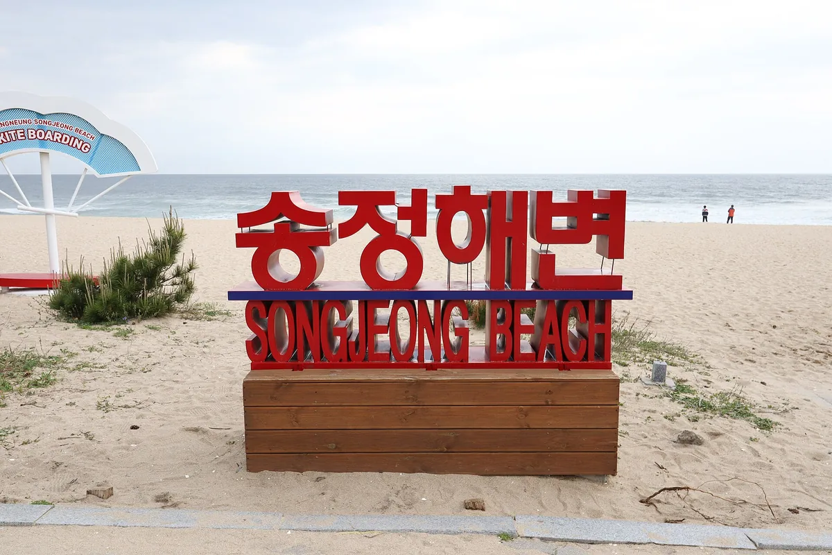 The red Songjeong Beach sign on the sand, facing the sea