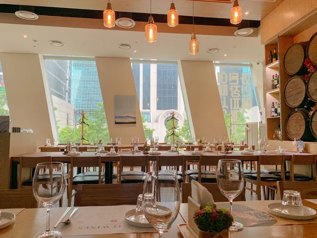Set tables with wine glasses facing tall windows, and wooden barrels on the wall