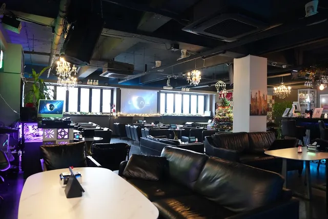 A wide lounge with black leather sofas, crystal chandeliers and large screens on the wall