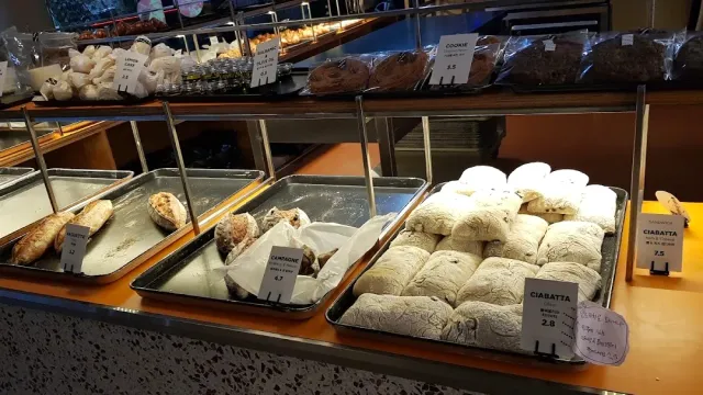 Trays of floured bread and pastries in a display counter, beside handwritten price labels
