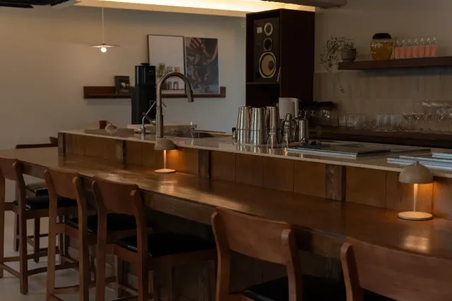 A long wooden counter with tall stools, shakers and small table lamps